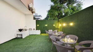 An outdoor patio with a dining area, artificial grass, wicker furniture, and string lights. - Itsy Hotels Vedansh (Ludhiana)