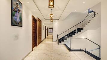 A hallway with a marble floor, wooden doors, a staircase with glass railings, and pendant lighting.