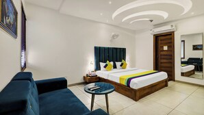 A modern hotel room with a bed, a sofa, a small round table, a ceiling fan, and an air conditioning unit. - Itsy Hotels Vedansh (Ludhiana)