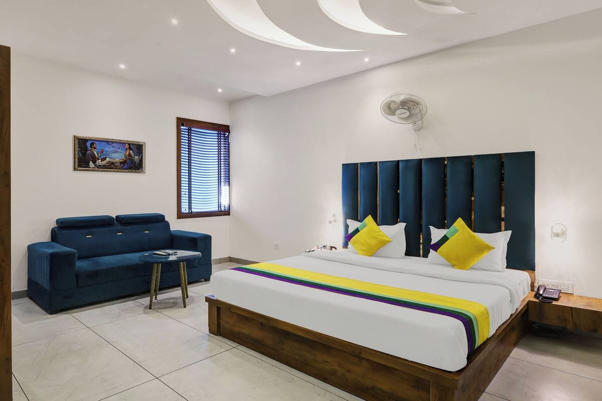 A modern bedroom with a large bed, a blue sofa, a small table, and a painting on the wall.