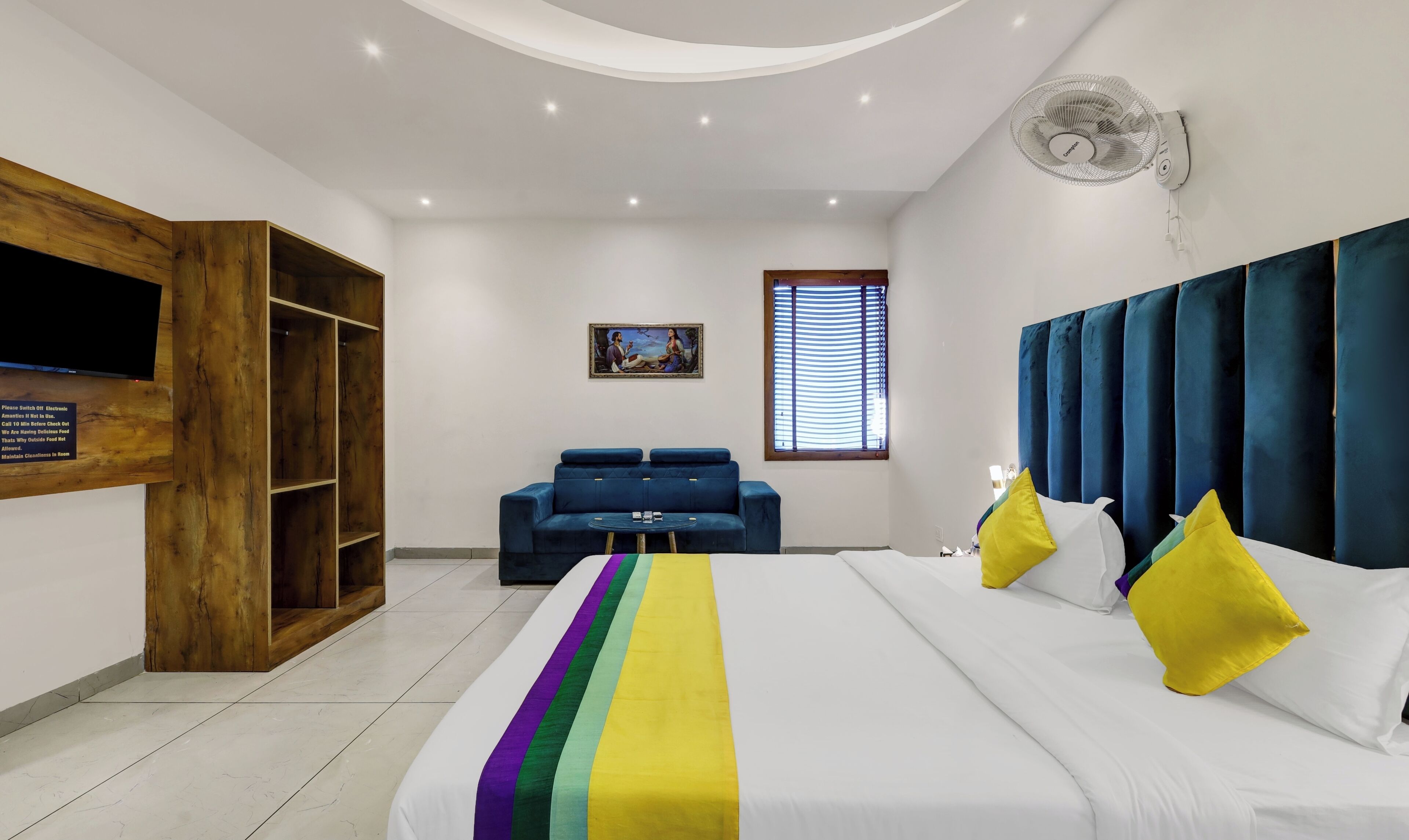 Un dormitorio moderno con una cama grande, un sofá azul, un armario de madera, un ventilador de techo y un cuadro en la pared.