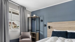 A hotel room with a bed, a chair, a desk, and a window with curtains.