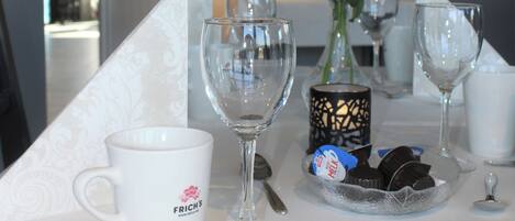 Una mesa de comedor dispuesta con una taza blanca, copas de vino, un florero con flores y una bandeja con bombones.