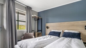 A bedroom with a bed, a nightstand, a window with curtains, and a view of greenery outside.