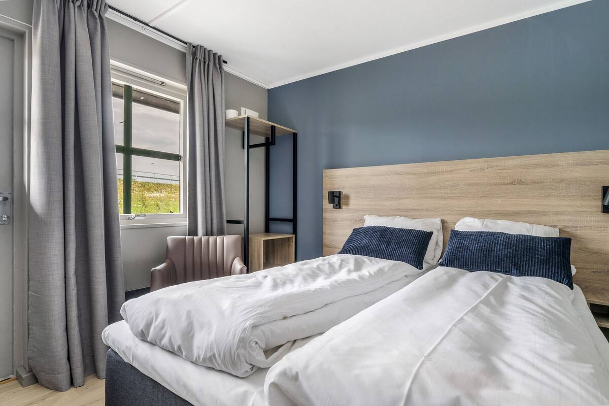 Un dormitorio con cama, una mesita de noche, una ventana con cortinas y vistas al exterior.