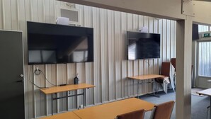 A conference room with two large flat-screen TVs mounted on the wall, wooden tables, and chairs.