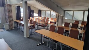 A conference room with tables and chairs, large windows, and a brick wall.