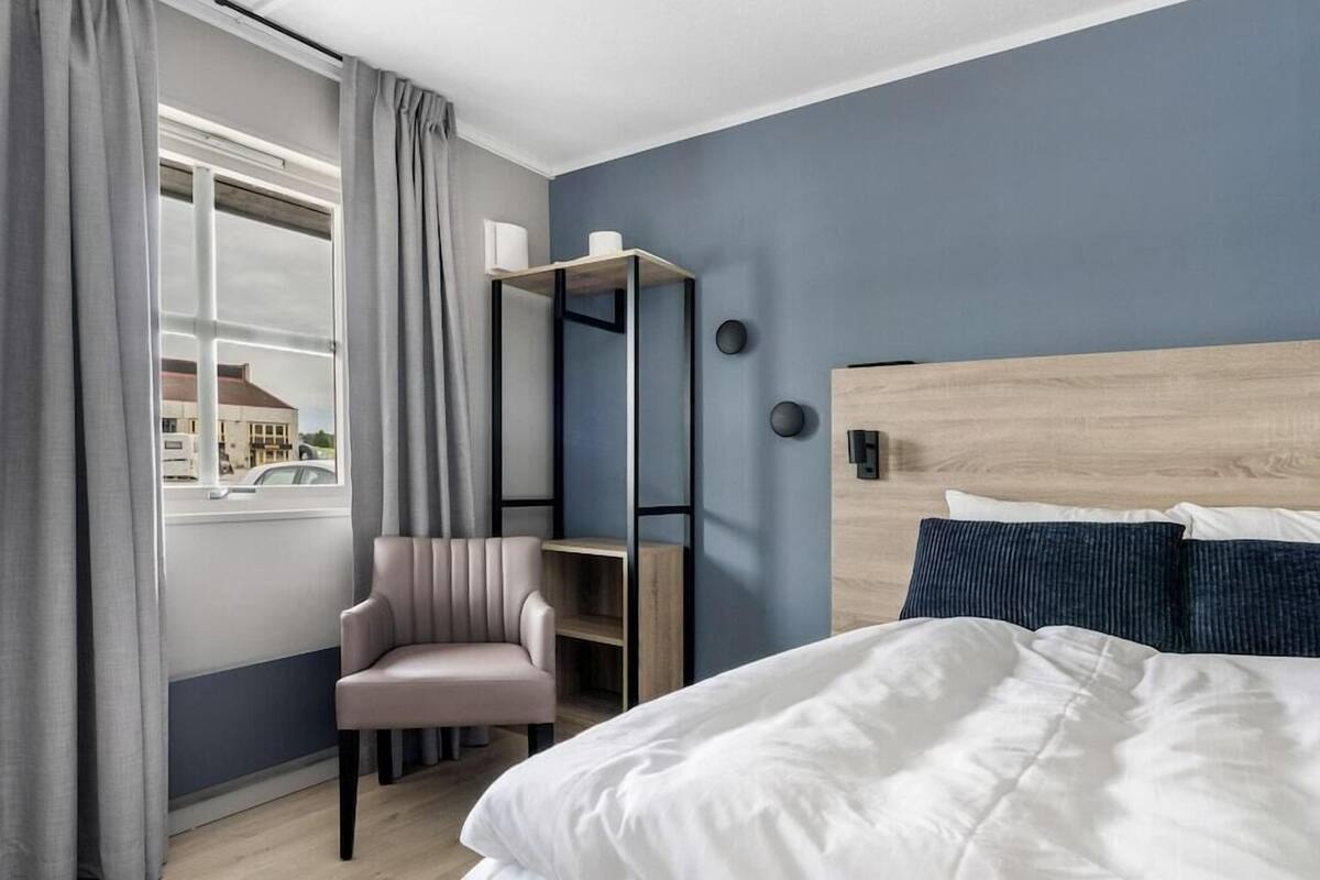 Una habitación de hotel con cama, una silla, un escritorio y una ventana con cortinas.