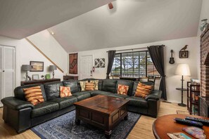 Una sala de estar con un sofá modular, una mesa de centro de madera, un tapete y una ventana con cortinas.