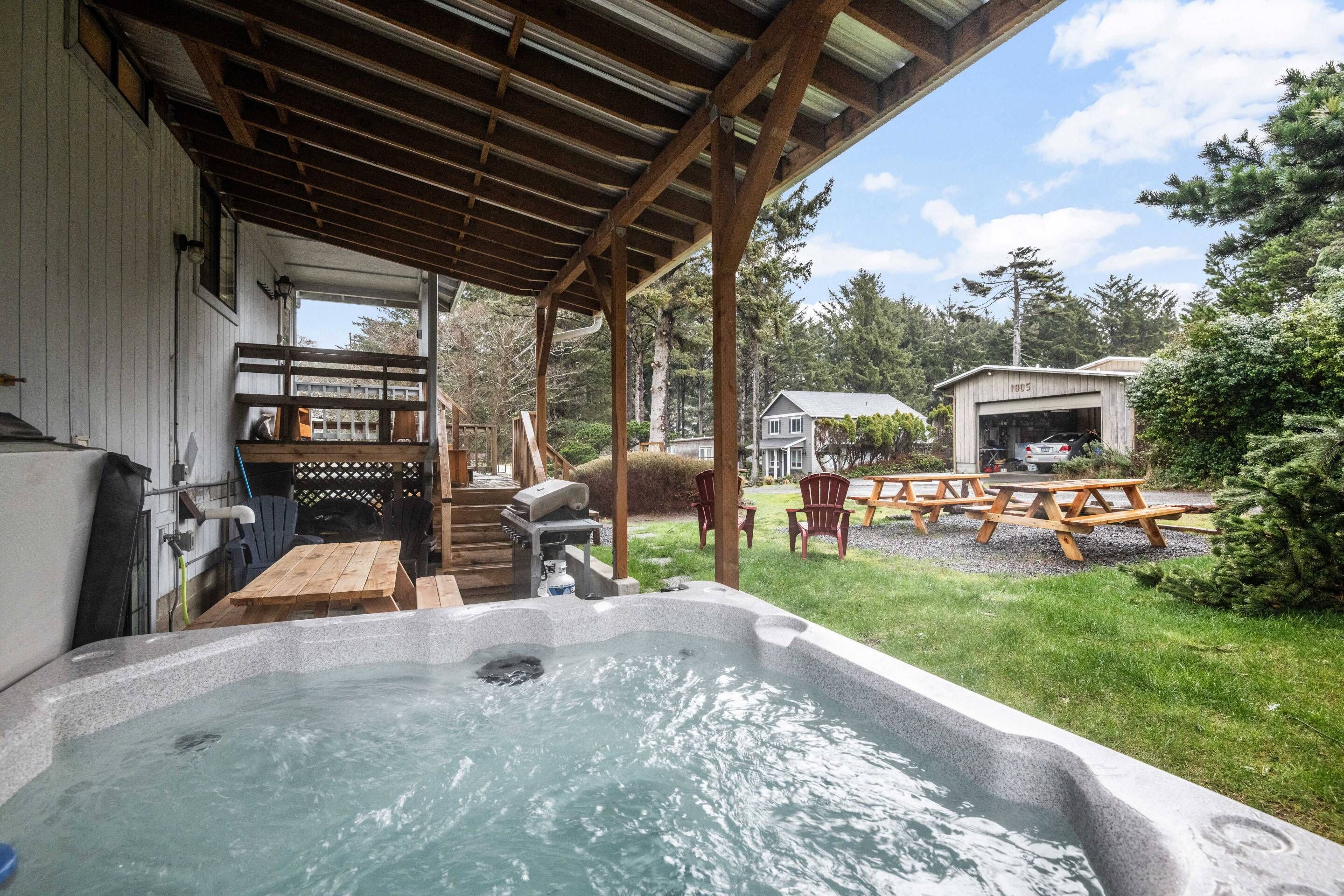 Un espace avec un jacuzzi, une terrasse en bois, des tables de pique-nique et un coin salon abrité.