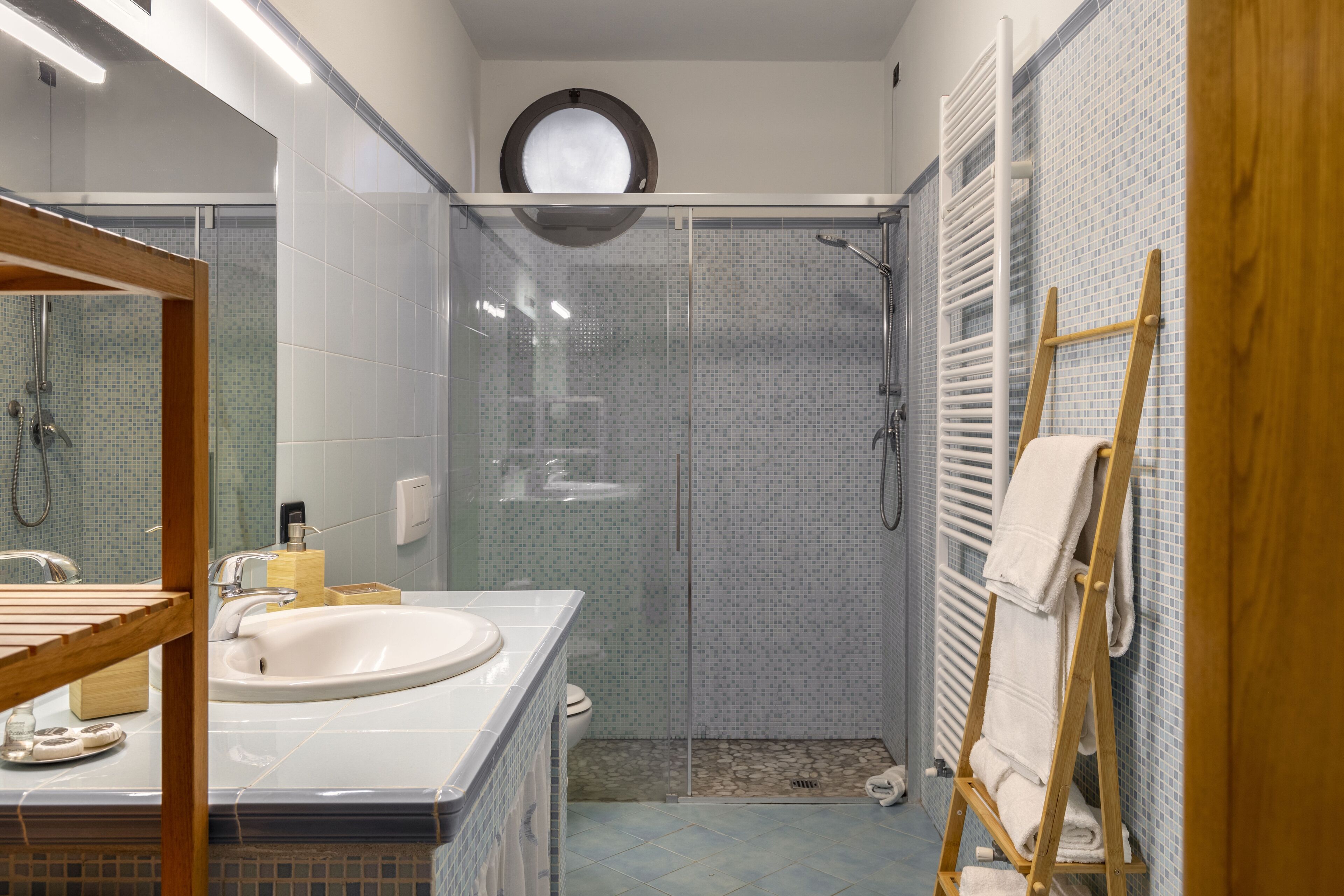 Une salle de bain avec une douche à parois de verre, un lavabo avec un miroir et un porte-serviettes en bois.