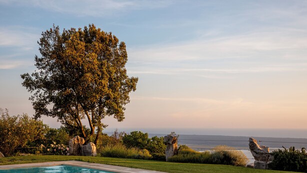 A swimming pool with a view of the ocean, surrounded by greenery and rocks. - House Geranio  in Tuscany (LUCCA) with Pool, garden and spectacular sea view  (Toscana)