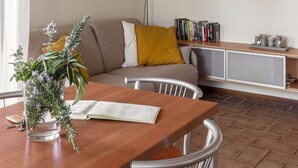 A cozy living room with a wooden dining table, a sofa with cushions, a bookshelf, and a wall clock. - House Geranio  in Tuscany (LUCCA) with Pool, garden and spectacular sea view  (Toscana)