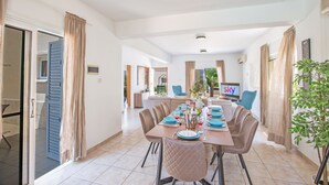 A dining area with a table set for six, a television in the background, and a plant on the right.