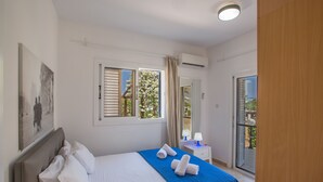A bedroom with a bed, a nightstand, a window with curtains, and an air conditioning unit.