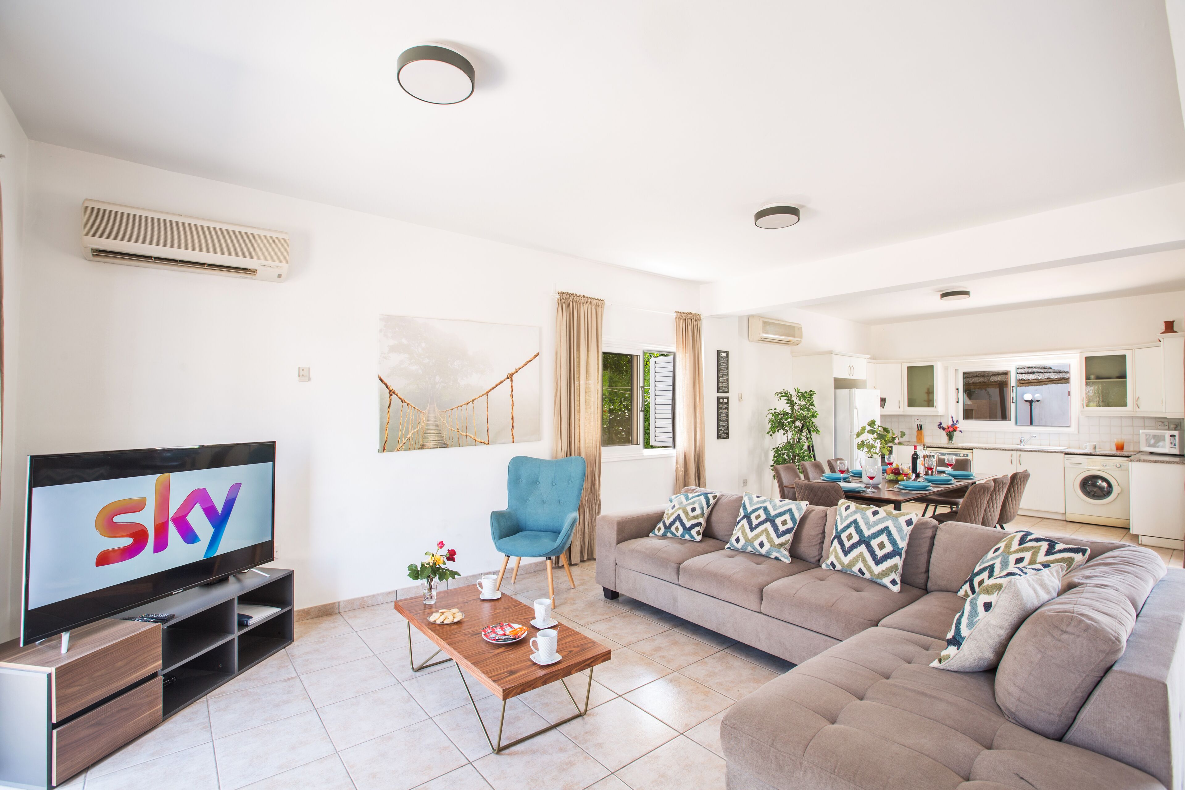 A modern living room with a flat-screen TV, a blue armchair, a beige sofa, and a wooden coffee table.