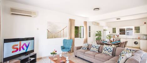 A modern living room with a flat-screen TV, a blue armchair, a beige sofa, and a wooden coffee table.