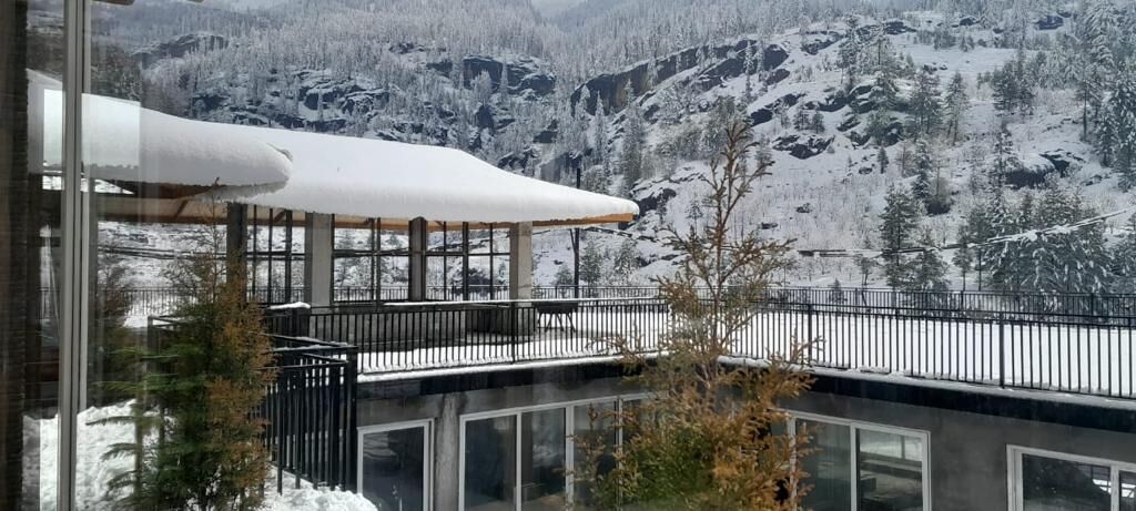 A modern building with a glass facade, a balcony with a metal railing, and a snowy mountainous backdrop.