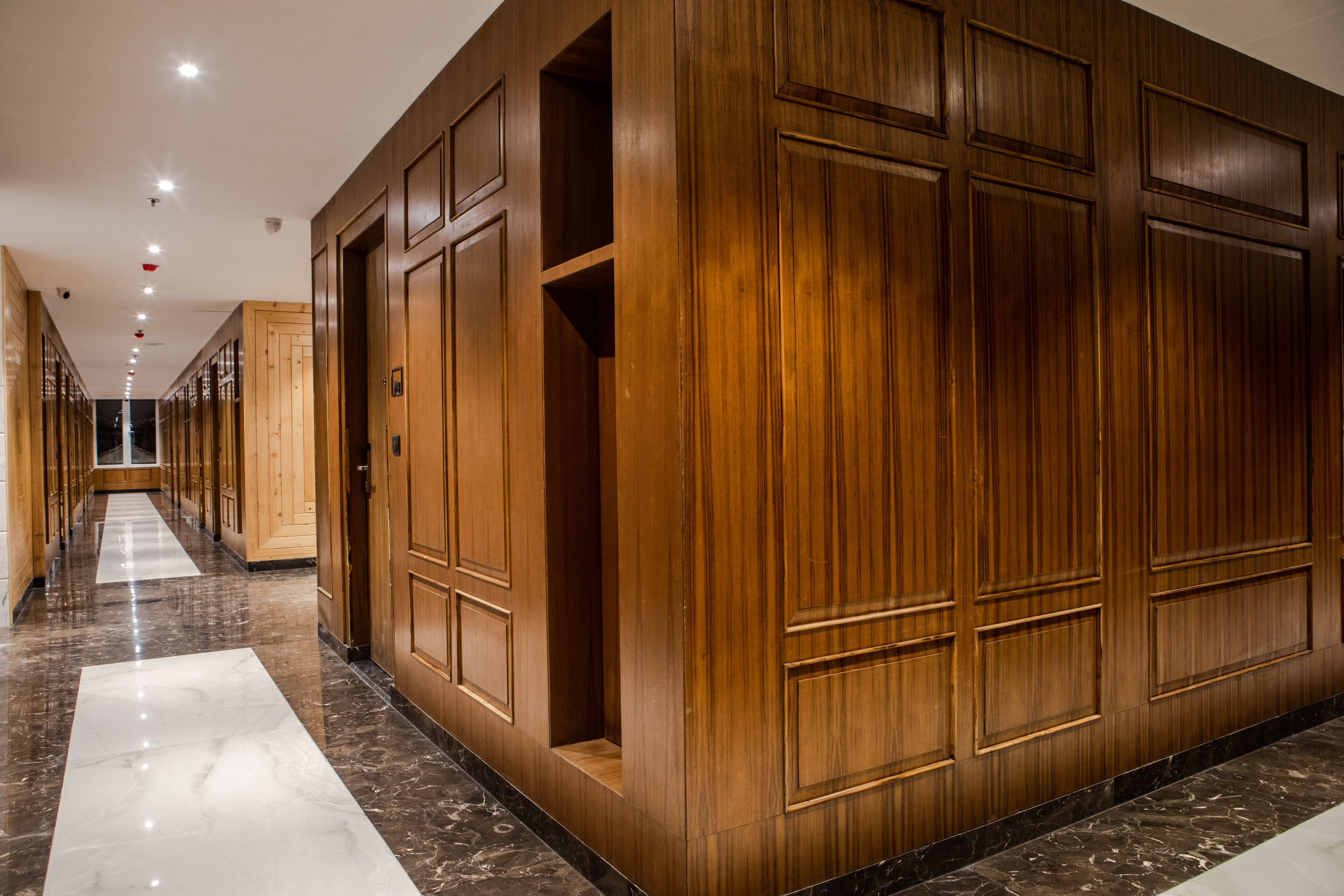 A long corridor with wooden paneling and marble flooring.