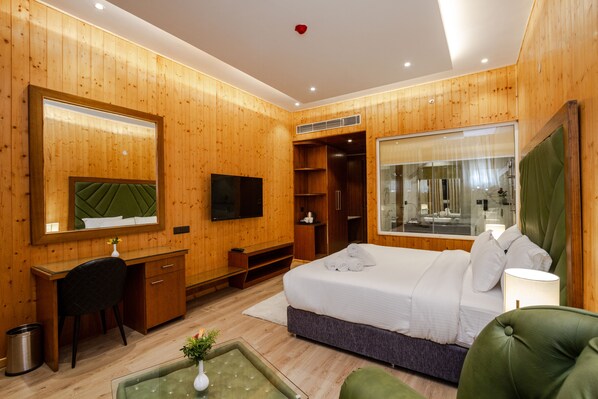 Una habitación de hotel moderna con paneles de madera, una cama grande, un escritorio, un televisor y un baño con cabina de ducha de vidrio.
