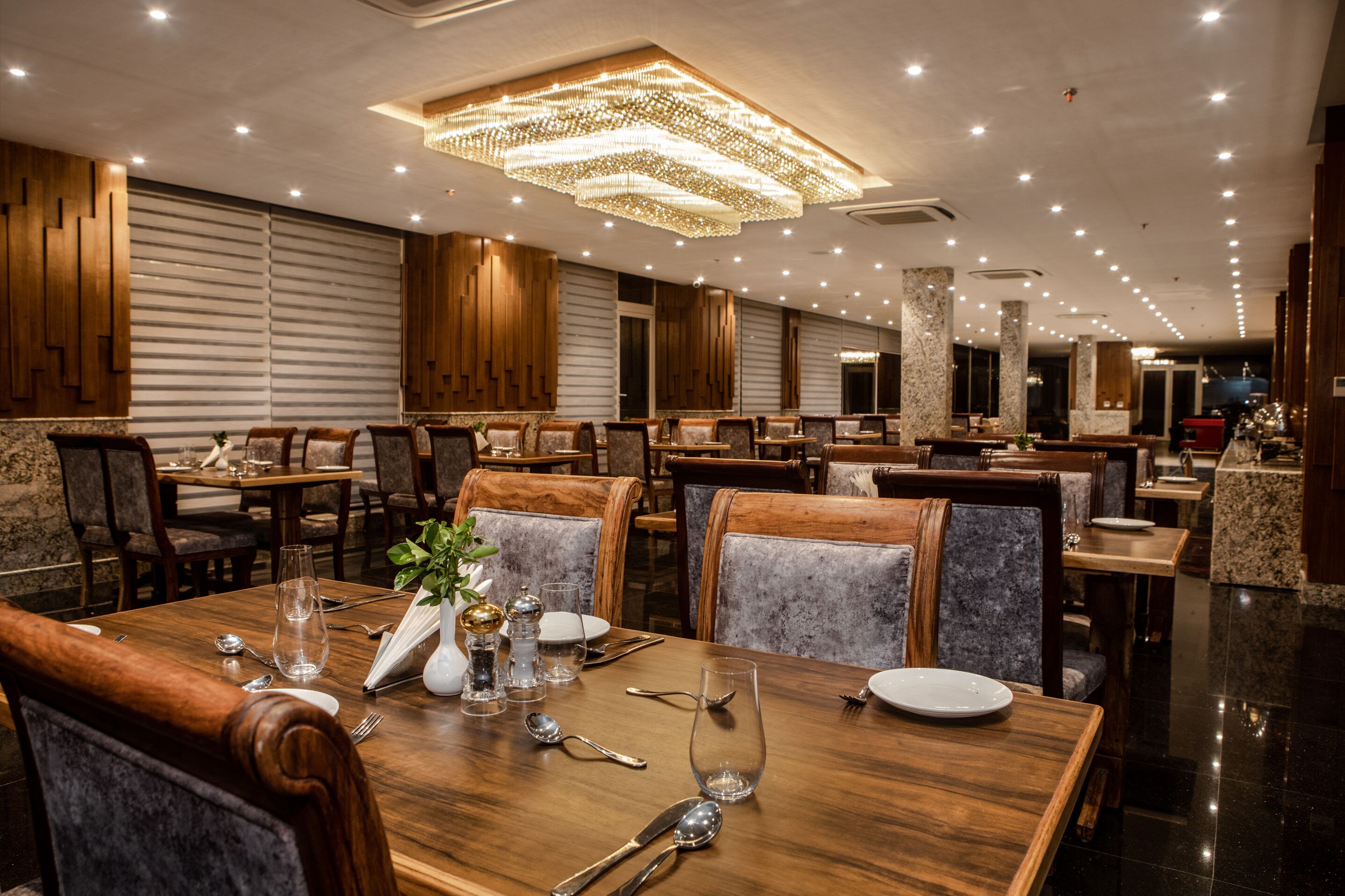 A well-lit restaurant with wooden furniture, marble accents, and a modern chandelier.