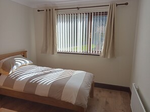 Een slaapkamer met een bed, een raam met zonwering en een radiator.