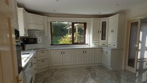 Una cocina moderna con armarios blancos, un ventanal grande y suelo de baldosas.