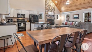 Uma cozinha moderna com armários brancos, lareira de pedra e sala de jantar com mesa e cadeiras de madeira.