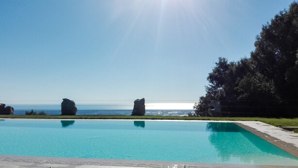 A swimming pool with clear blue water, surrounded by a grassy area and large rock formations. - House Girasole in the country with Pool, garden and spectacular sea view  (Toscana)