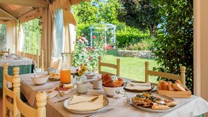 A breakfast table set with plates, cutlery, and a variety of food items, including pastries and a glass of orange juice, in a tented outdoor dining area with a garden view. - House Girasole in the country with Pool, garden and spectacular sea view  (Toscana)