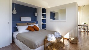 A bedroom with a bed, pillows, a bedside table with towels, a bookshelf, a mirror, and a dining area with chairs and a table. - House Girasole in the country with Pool, garden and spectacular sea view  (Toscana)