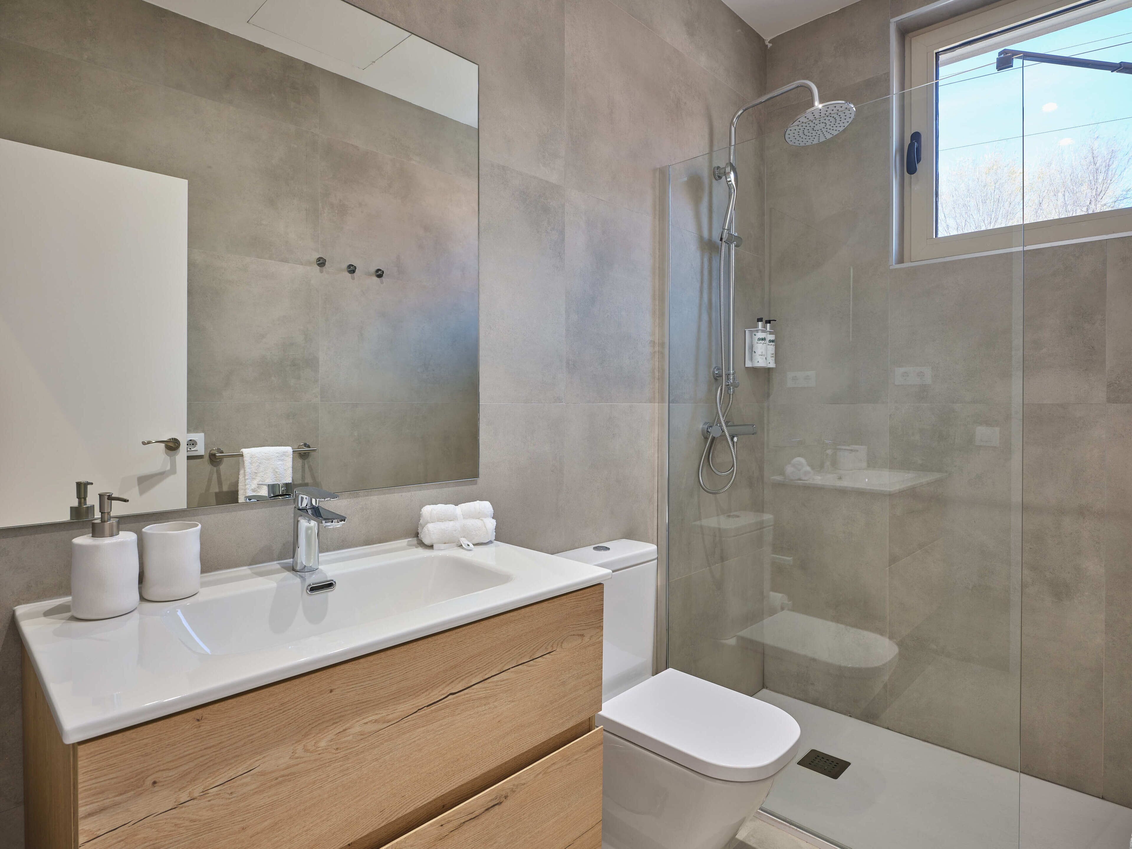 A modern bathroom with a glass-enclosed shower, a white sink with a wooden vanity, and a large mirror.