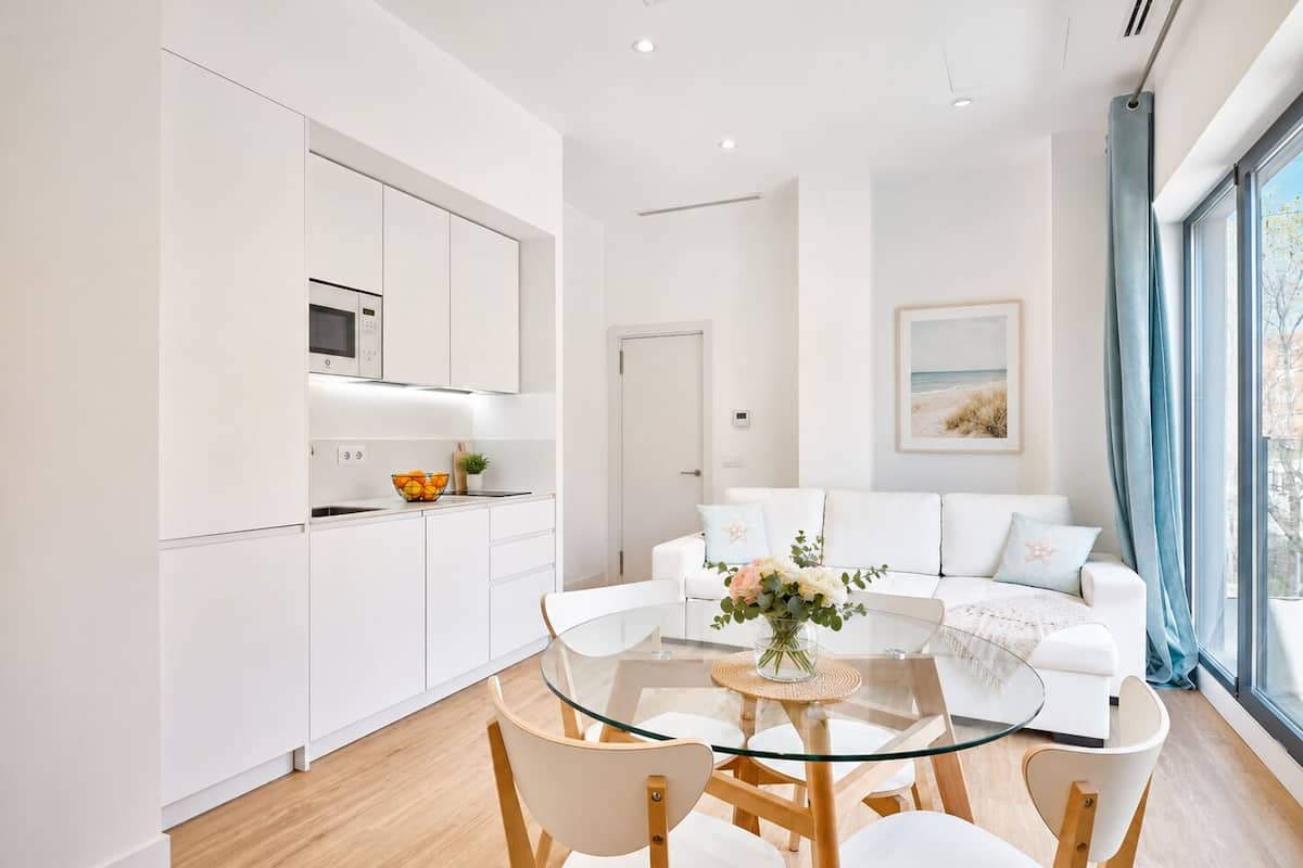 A modern kitchen with white cabinetry, a glass dining table, and a white sofa in the living area.