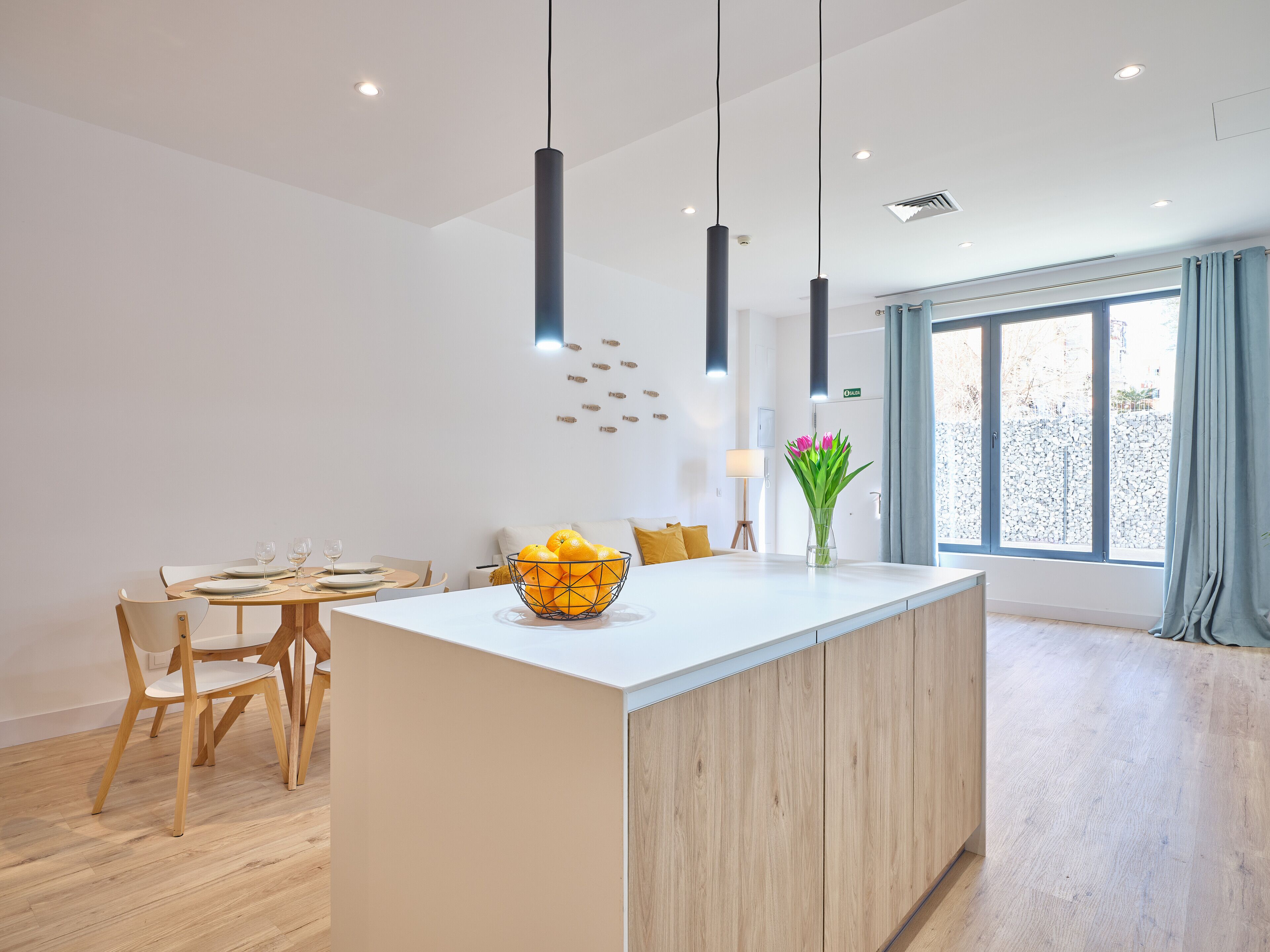A modern kitchen with a central island, wooden chairs, and a dining table set for two.