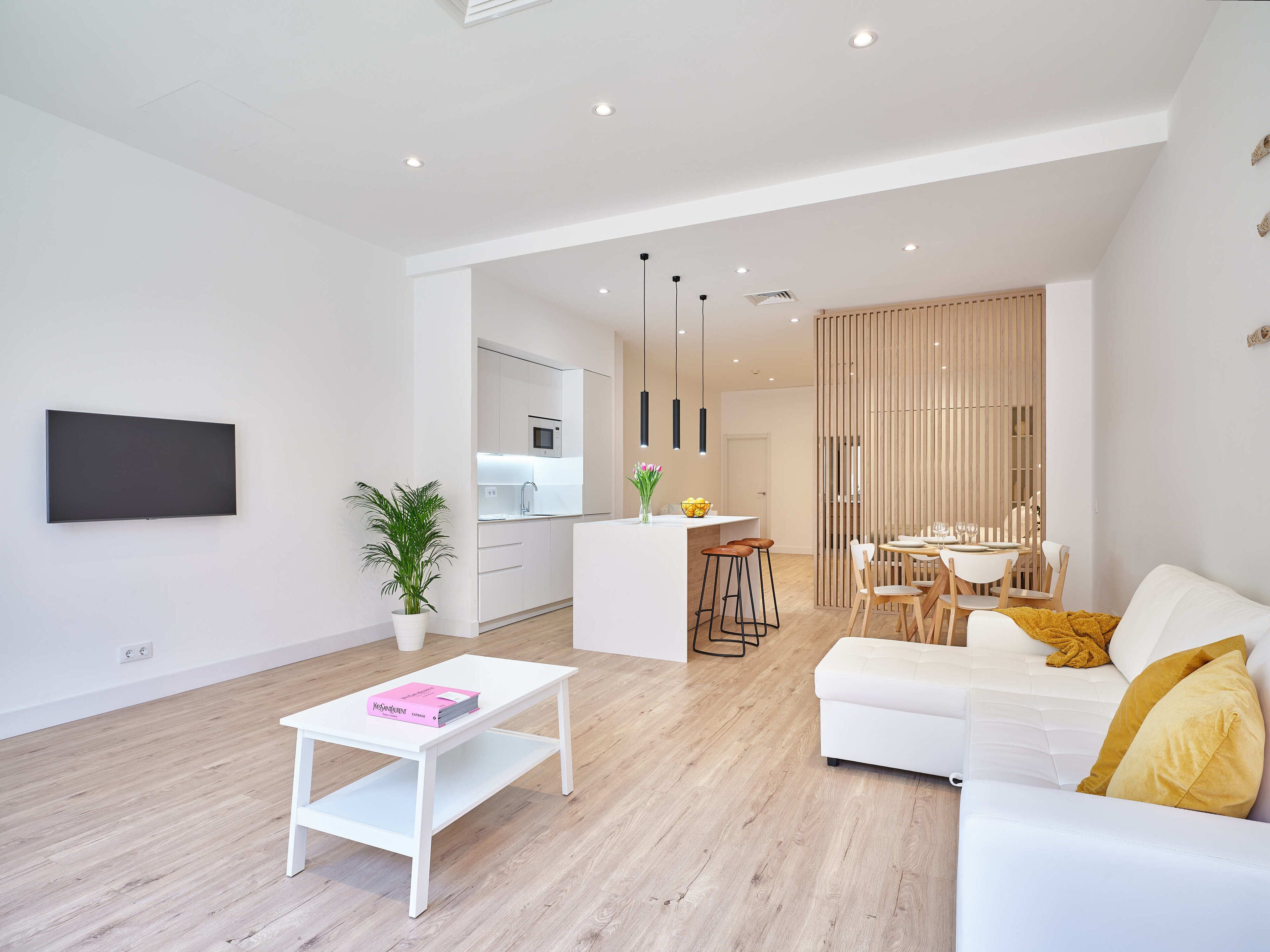 Una sala de estar moderna con un sofá blanco, una mesa de centro y un comedor con mesa y sillas de madera.