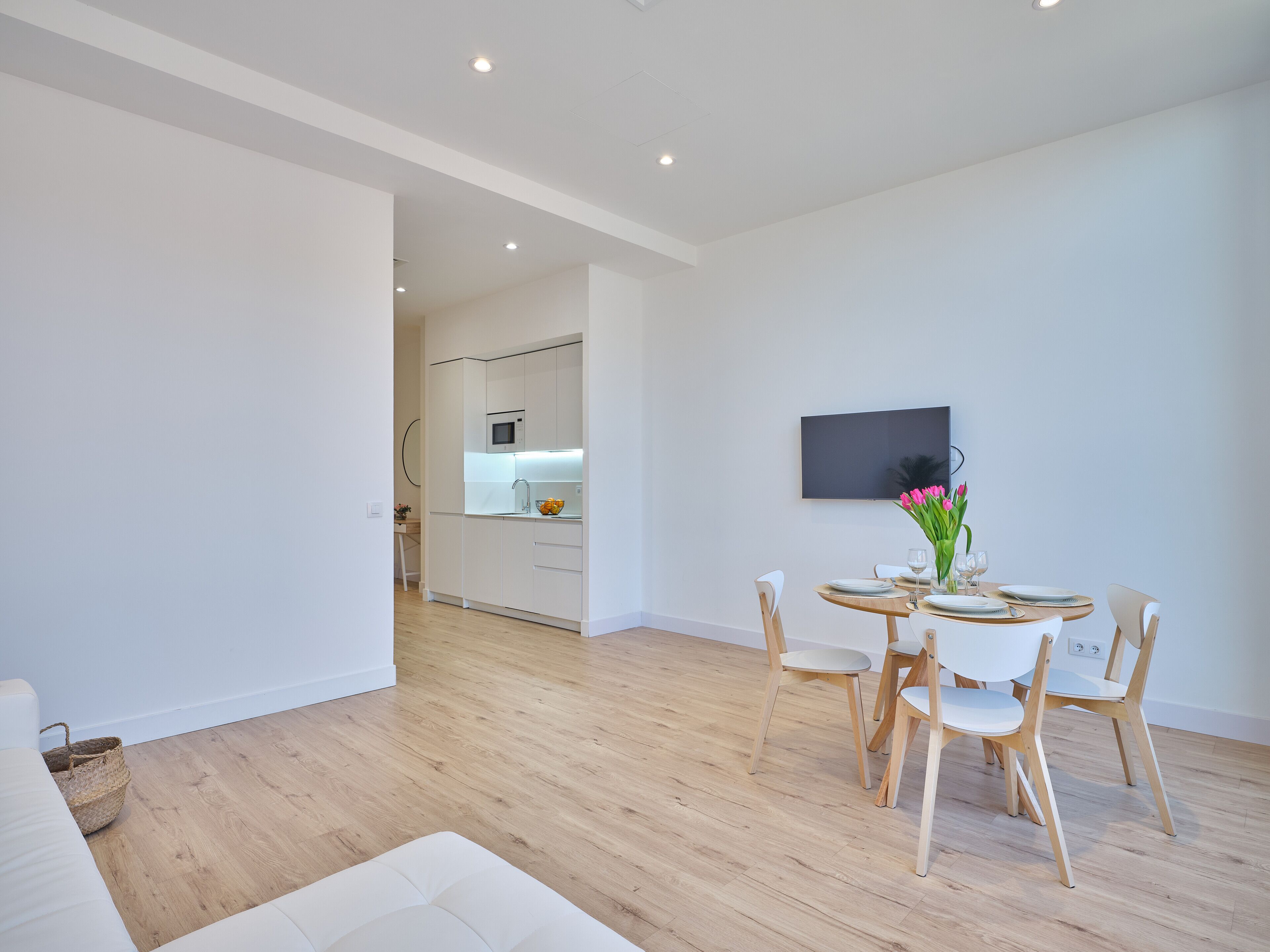 Una sala moderna con comedor, suelo de madera y una cocina al fondo.