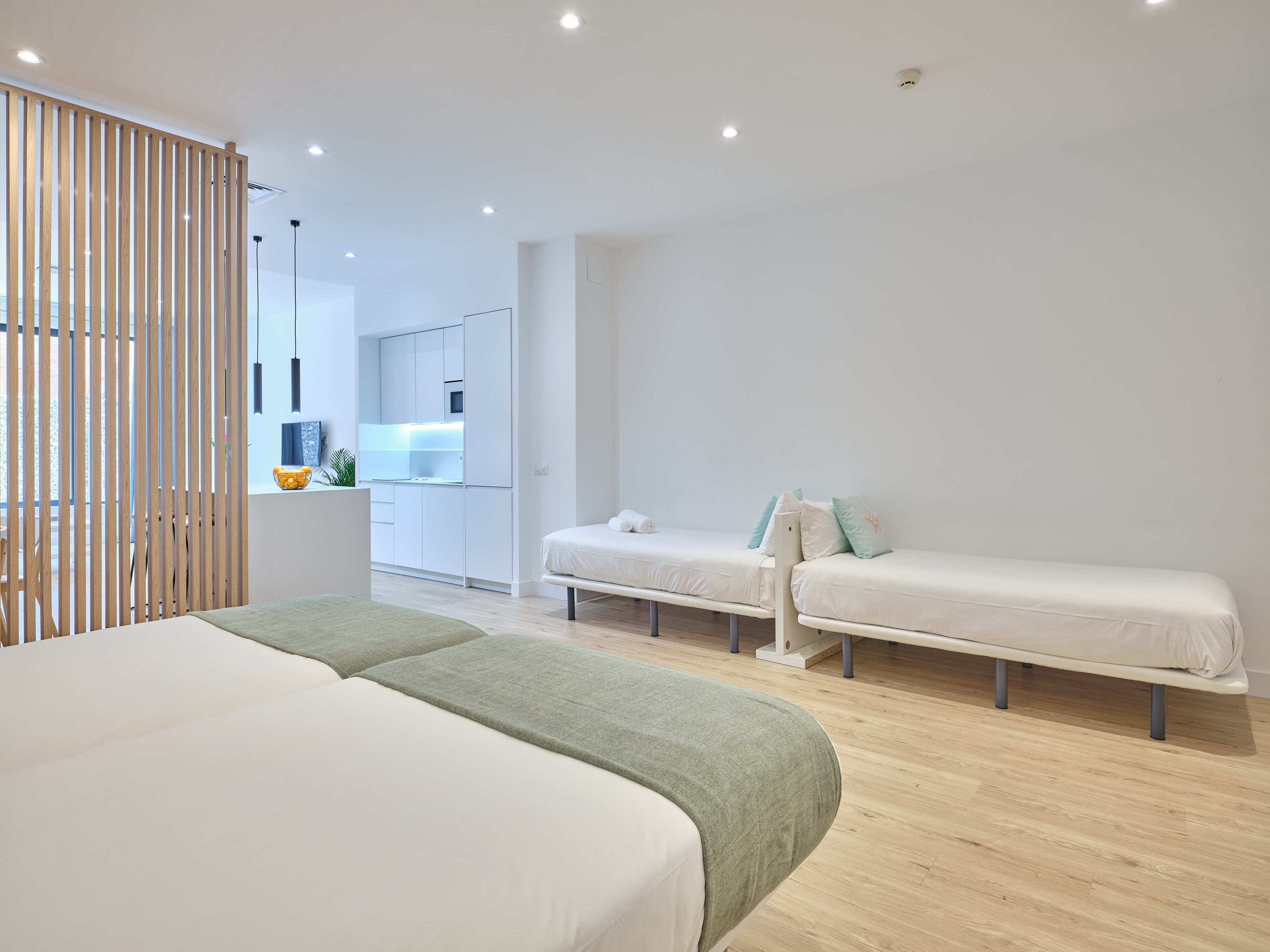 Habitación de hotel moderna con una cama grande, dos camas más pequeñas, una zona de cocina y vistas a la ciudad.