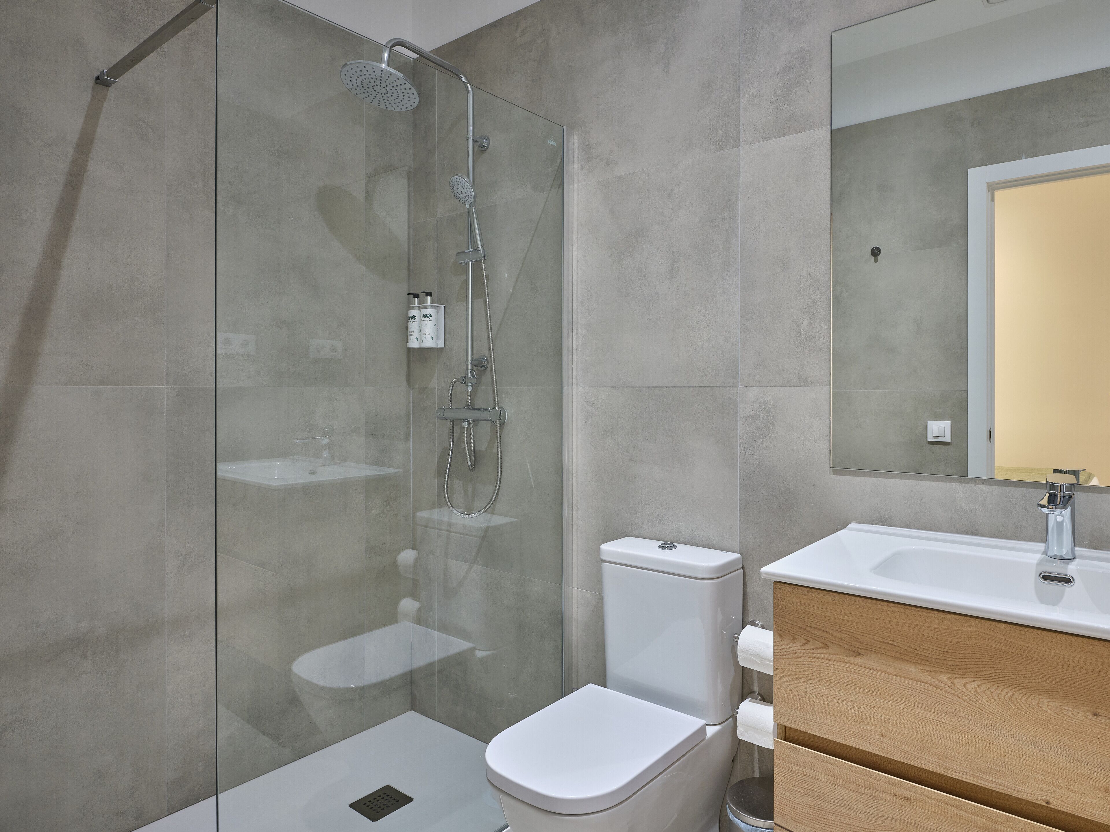 A modern bathroom with a glass-enclosed shower, a toilet, and a vanity with a mirror.