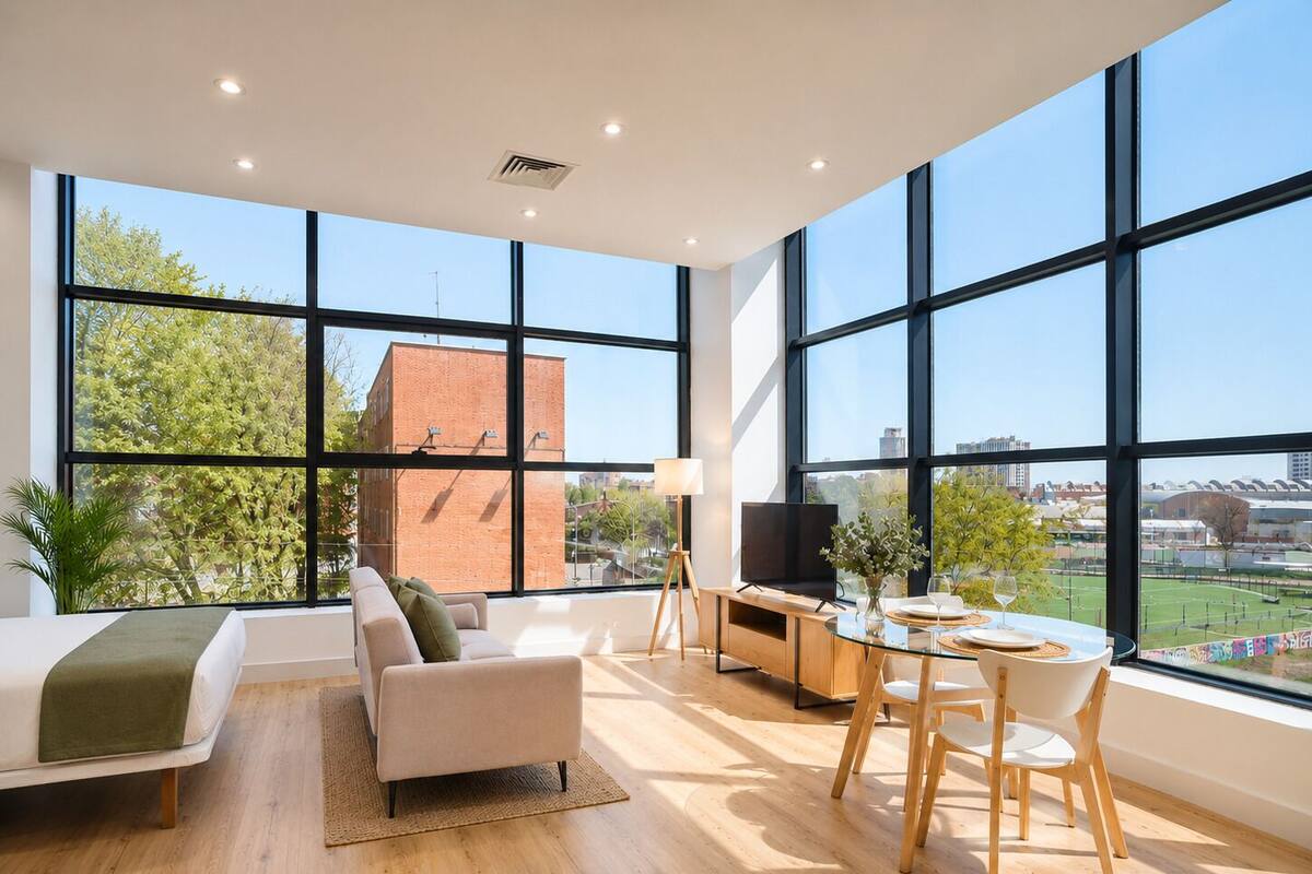 A spacious room with large windows, a sofa, a dining table with chairs, a TV, and a lamp.
