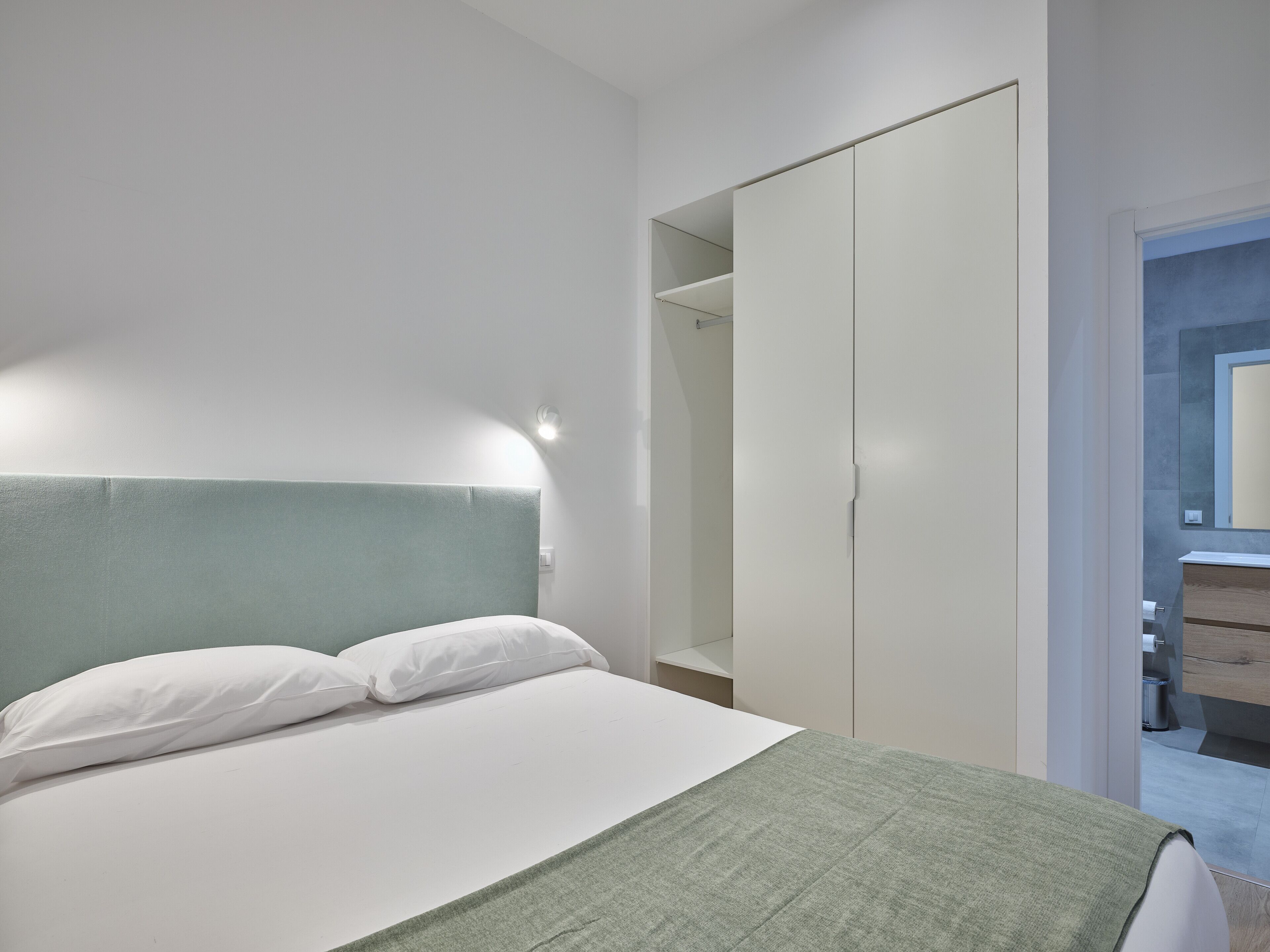 Una camera da letto moderna con un letto, un armadio e un bagno visibile attraverso una porta aperta.