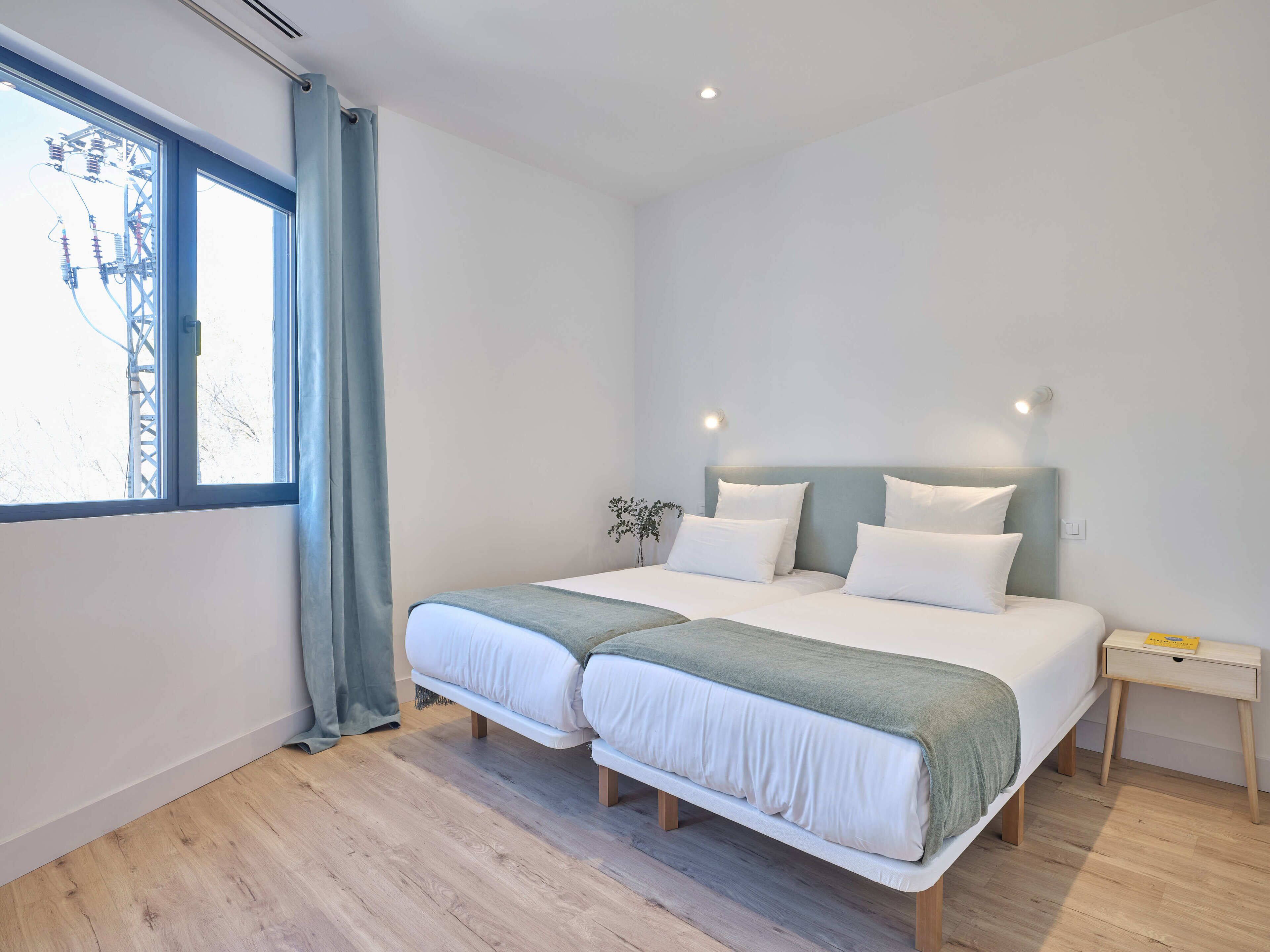 Un dormitorio moderno con un ventanal grande, una cama con ropa de cama blanca, una mesita de noche y una planta pequeña.