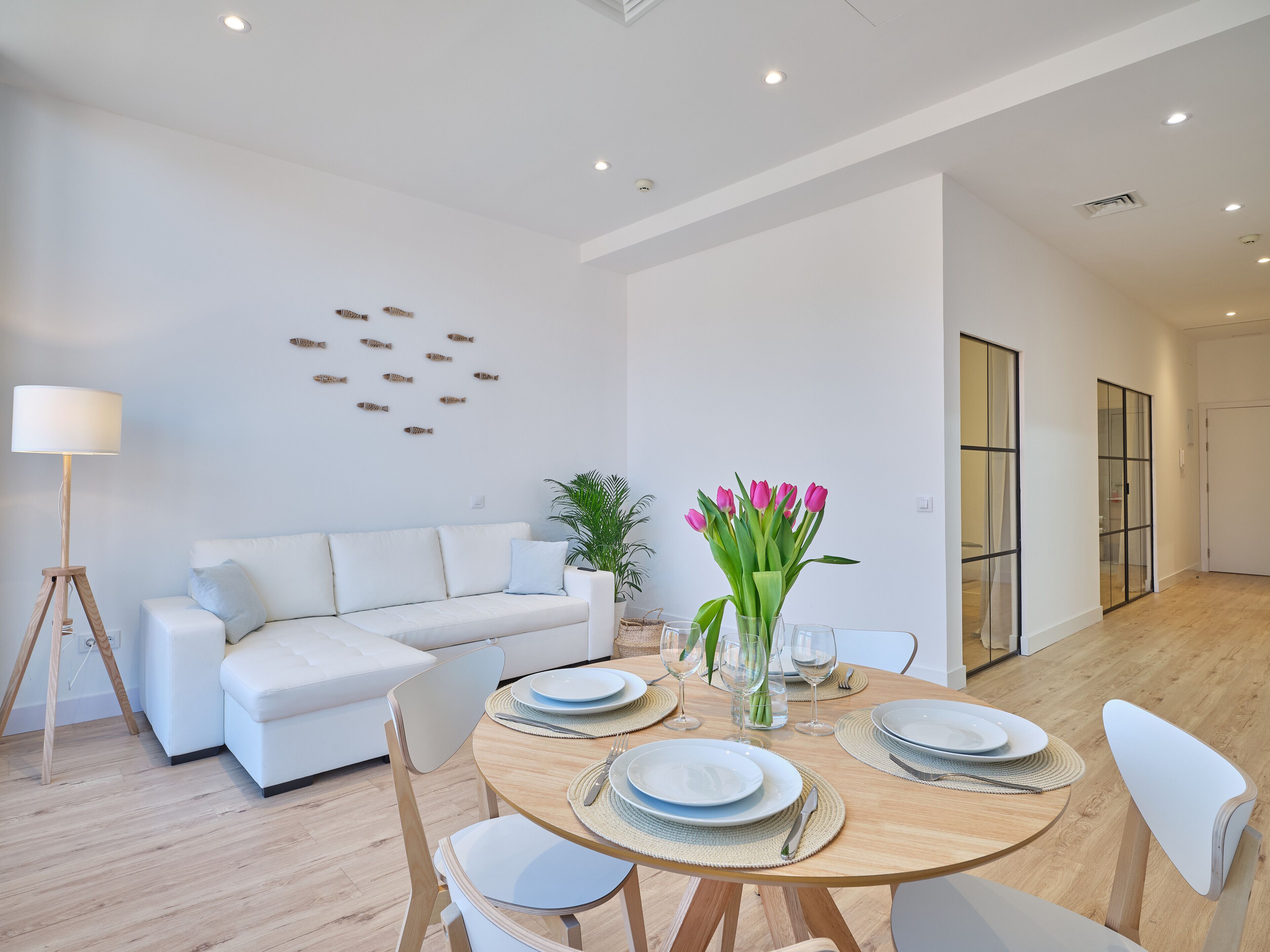 A modern living room with a white sofa, a dining table set with plates and glasses, and a floor lamp.