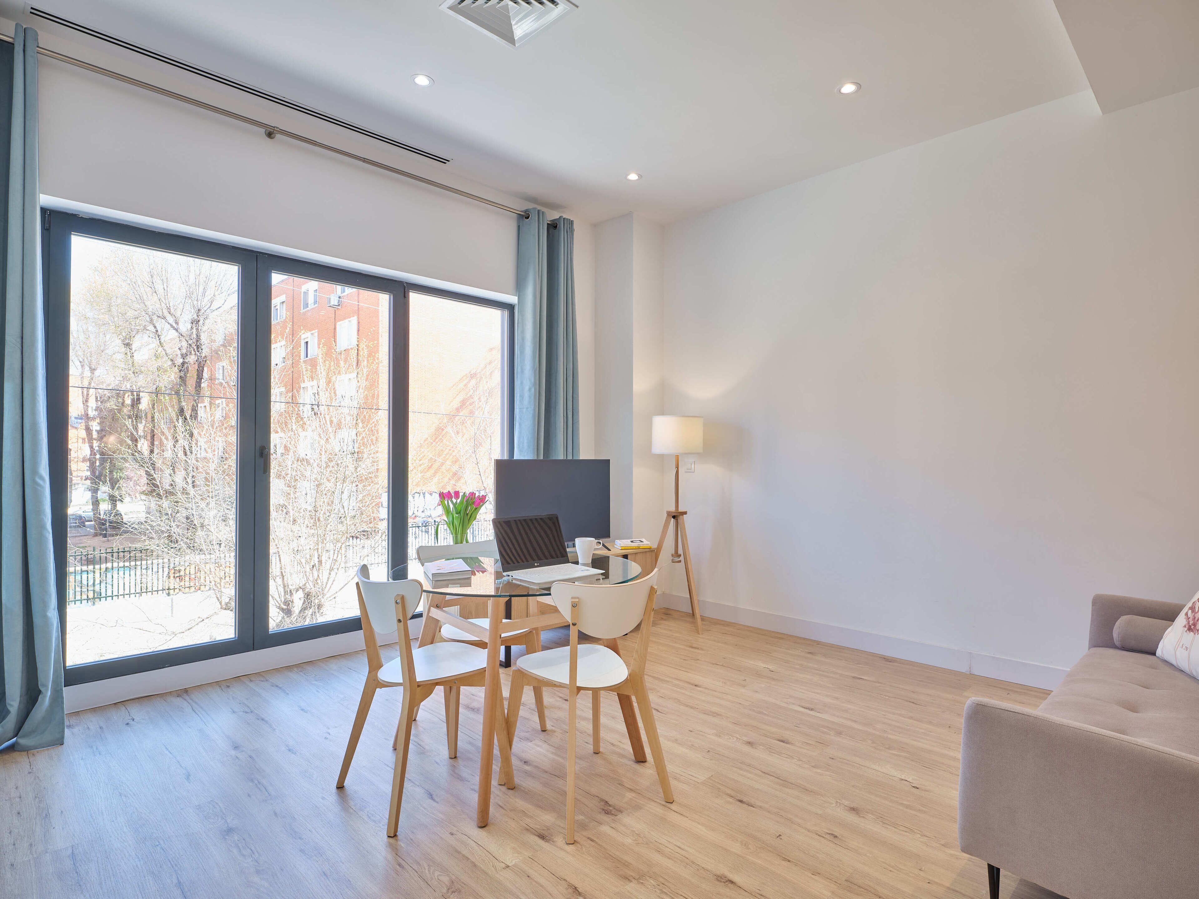 Una sala de estar moderna con una mesa de comedor de vidrio, sillas de madera, un sofá y una lámpara de pie.