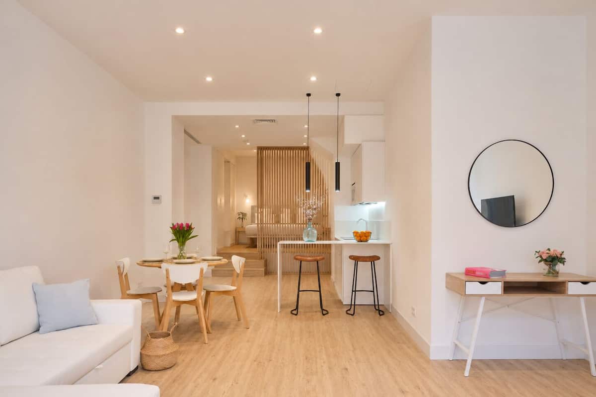 A modern living room with a sofa, dining table, and kitchen area with stools.