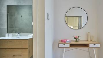 Un baño moderno con un espejo grande, un tocador de madera y un pequeño escritorio con un florero y libros.