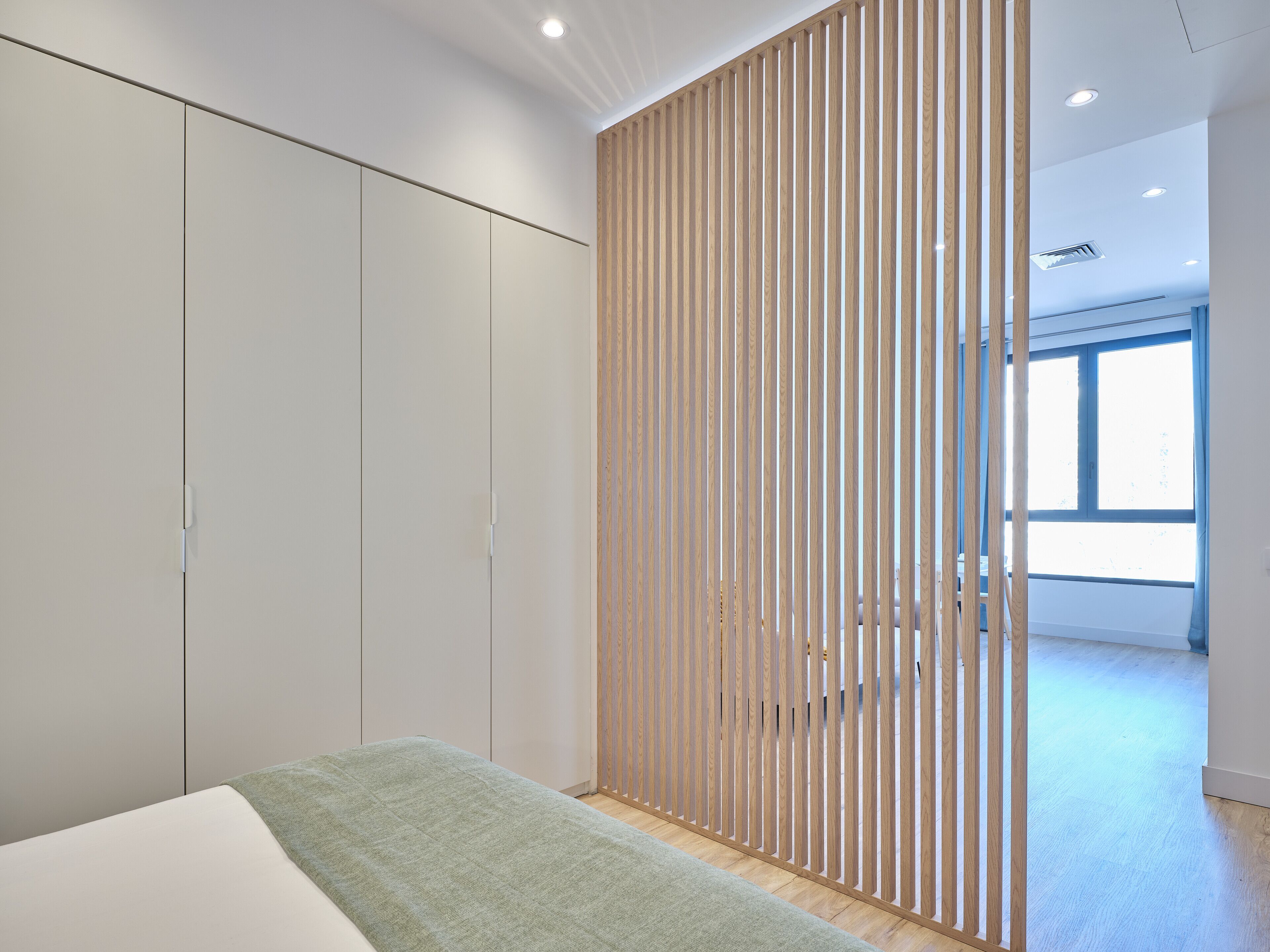 A modern bedroom with a large wardrobe, a wooden partition, and a large window.
