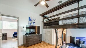 A bunk bed room with a TV on a dresser, wooden flooring, and a ceiling fan.