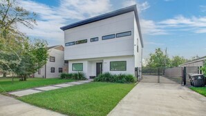A modern two-story house with a well-maintained lawn, a gated driveway, and a clear sky.