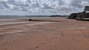 A beach with a stone wall and a pier in the background.
