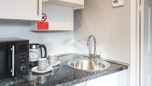 A modern kitchen with a stainless steel sink, a microwave, and a coffee maker. There is a 'No smoking' sign on the wall.